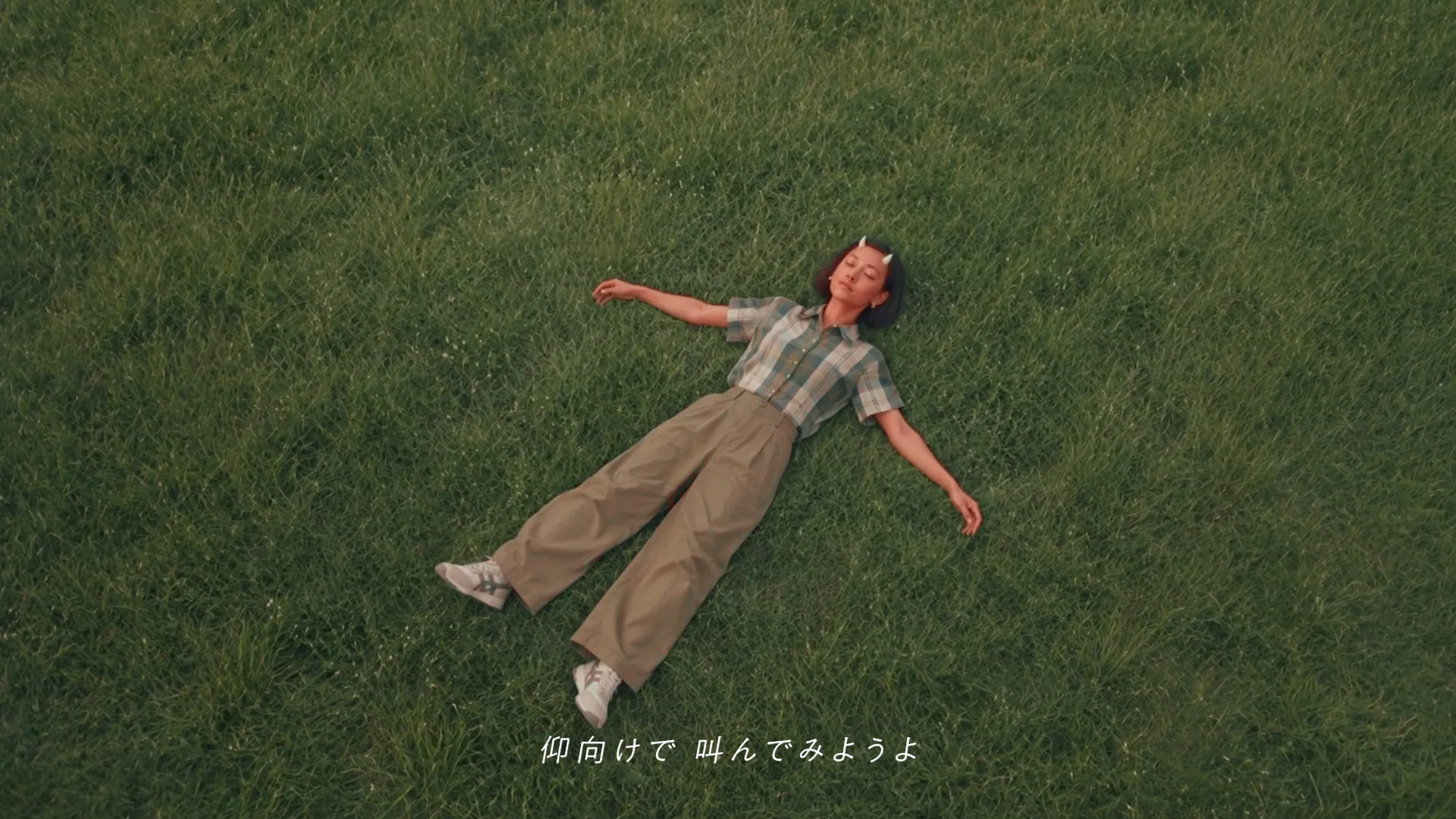 草の上で仰向けになるぐら。『仰向けで 叫んでみようよ』という字幕のMVカット